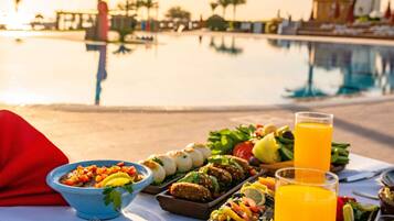 A dining table with various dishes, a glass of orange juice, and a pool in the background.