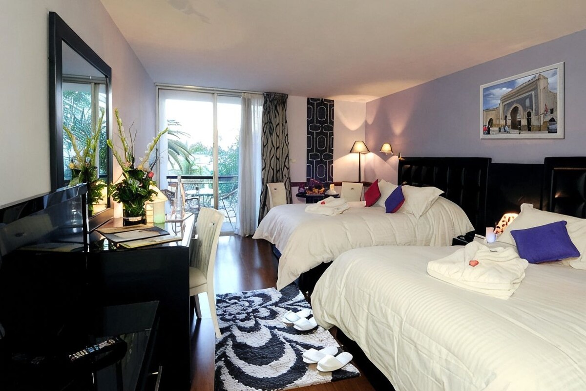 Habitación de hotel con dos camas, un escritorio, una silla, vistas al balcón y un espejo grande.