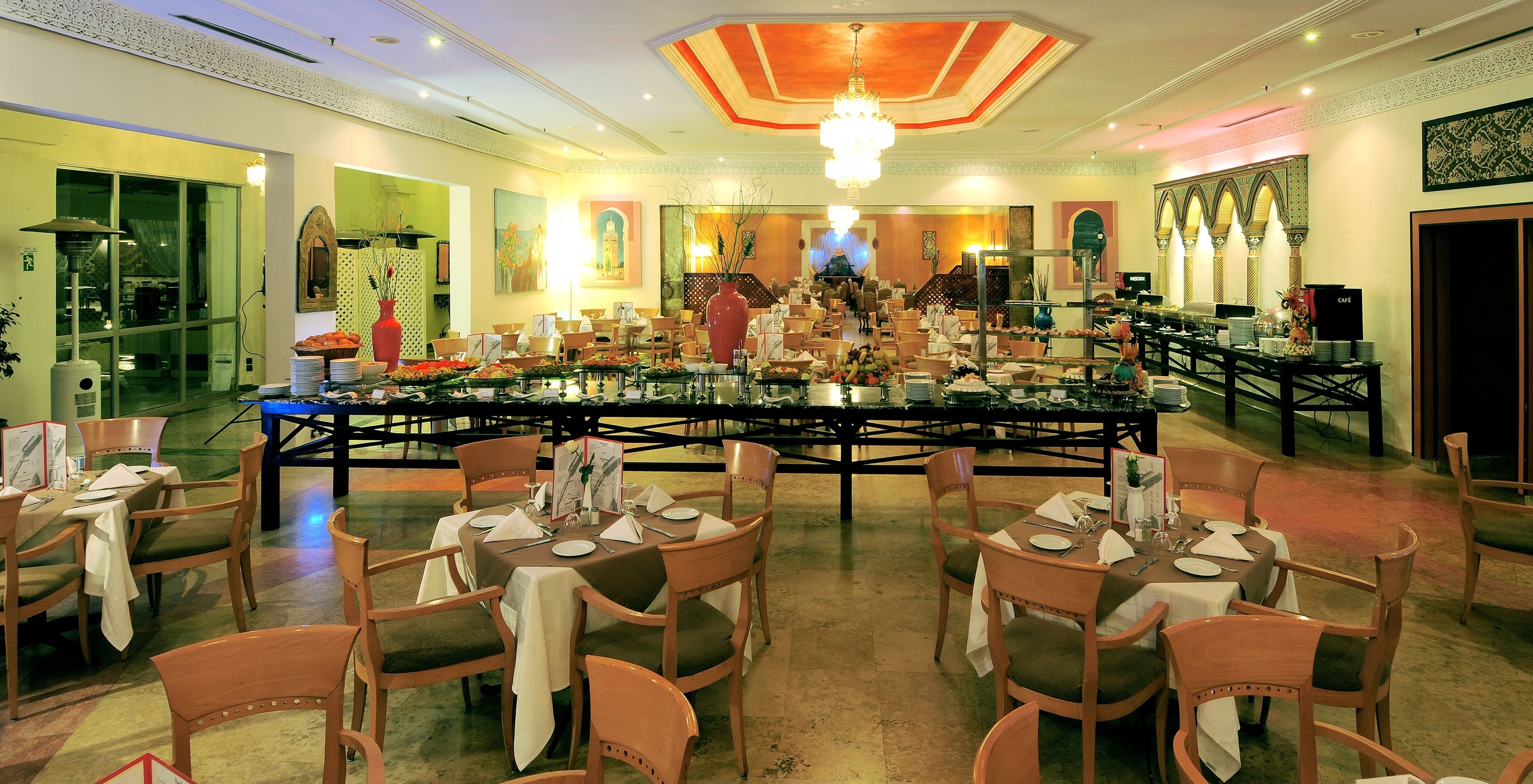 A spacious dining area with multiple tables and chairs, a chandelier, and decorative wall art.