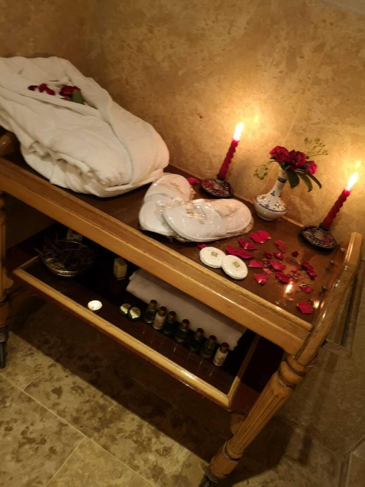 Un banco de madera con toallas, velas y un jarrón de flores en una habitación con pared texturizada.
