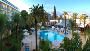 Zona de piscina de hotel con tumbonas, sombrillas y palmeras.