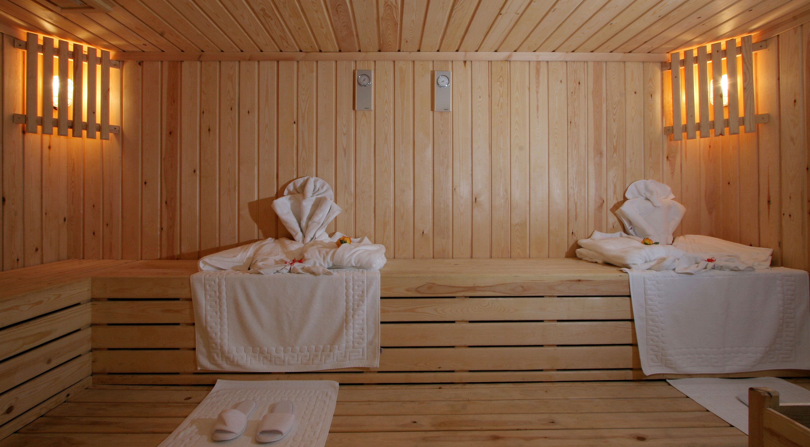 A sauna room with wooden benches and benches, towels, and a pair of slippers on the floor.