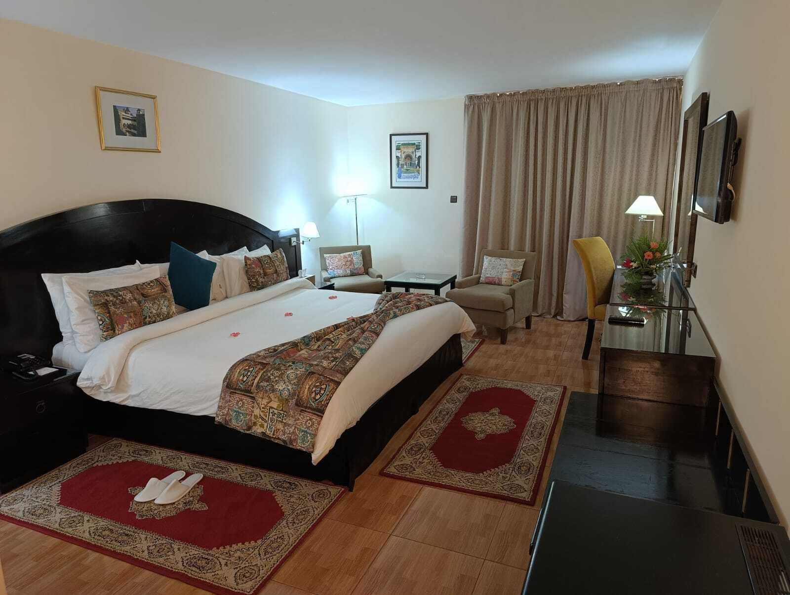 A hotel room with a large bed, a desk, a chair, a TV, and a window with curtains.