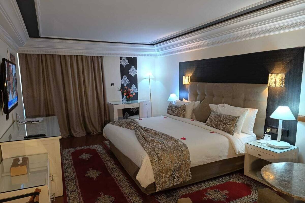 A hotel room with a large bed, bedside tables with lamps, a desk, and a TV.