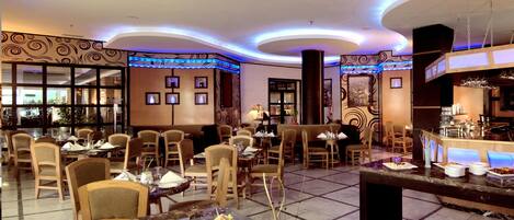 A spacious hotel dining area with multiple tables and chairs, a bar, and a buffet.