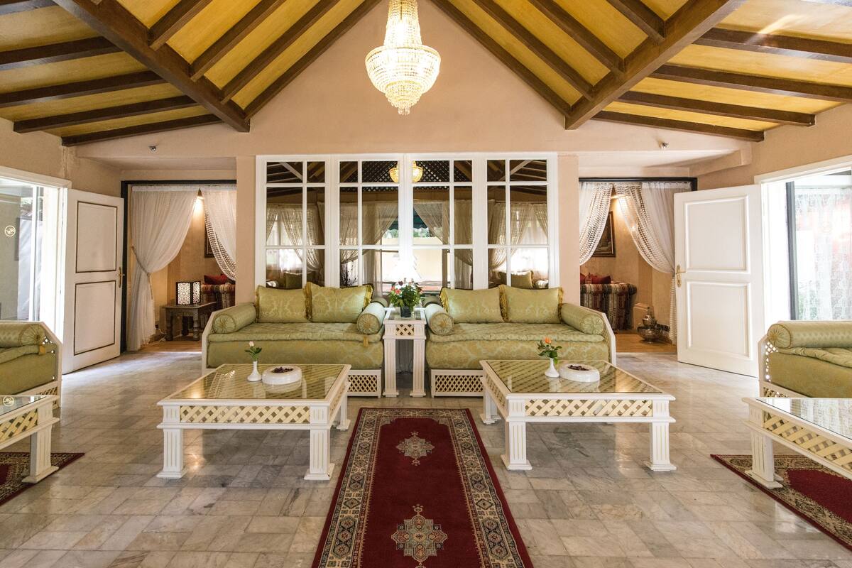 A spacious living room with two green sofas, white coffee tables, and a chandelier.