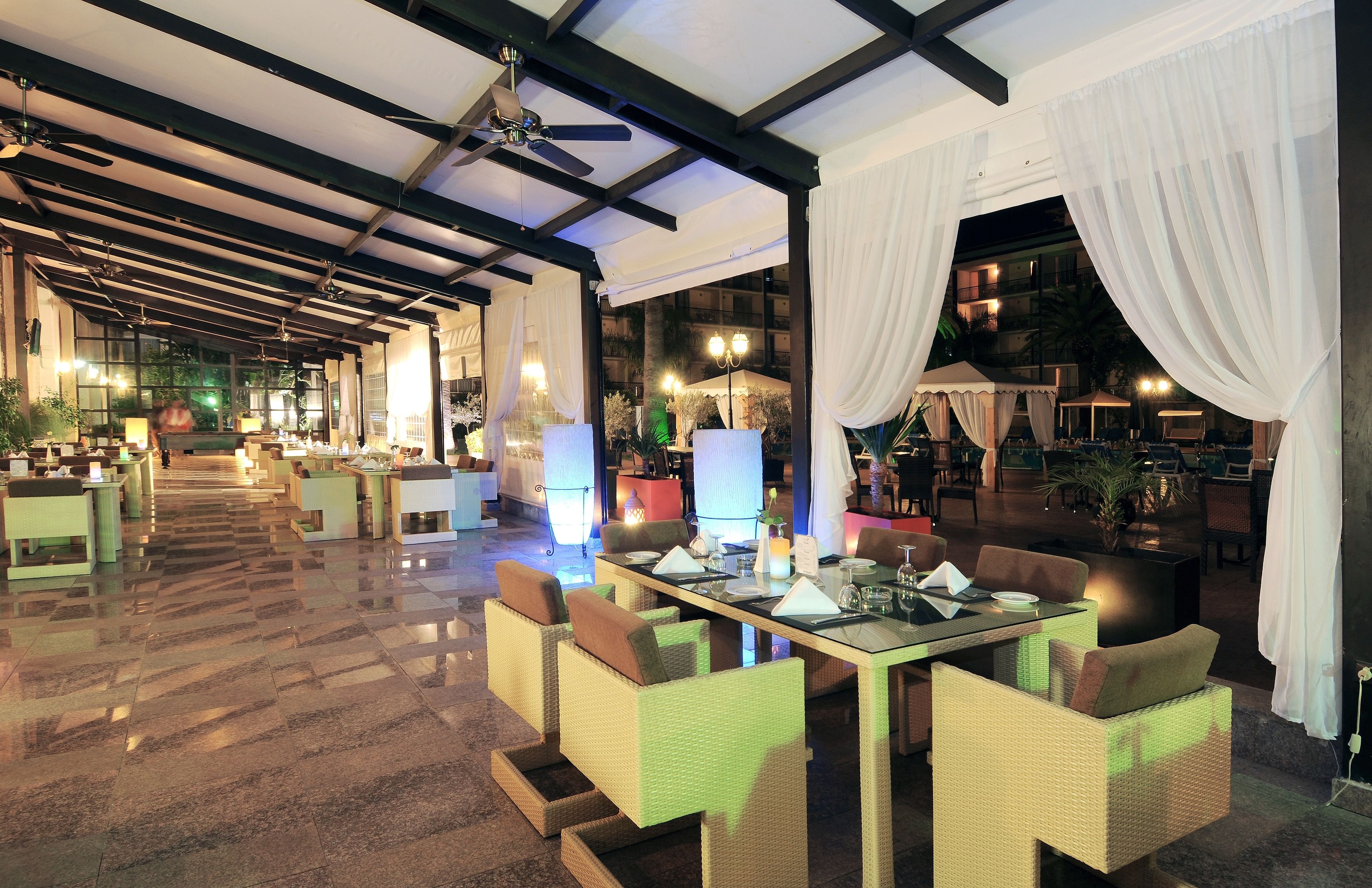 A spacious indoor dining area with high ceilings, chandeliers, and a long table set for dining.