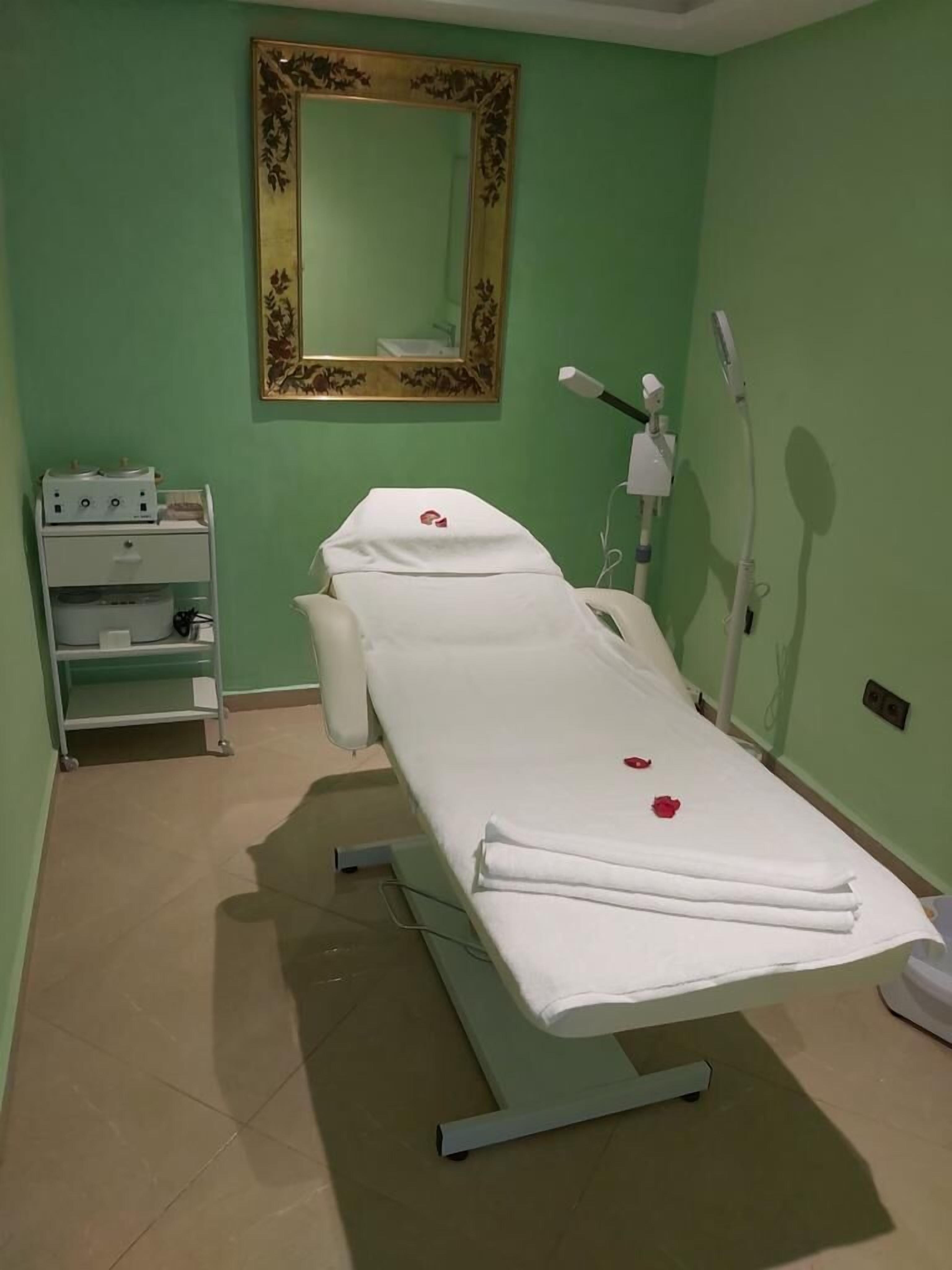 Un consultorio médico con una cama, un armario con equipo médico y un espejo grande en la pared.