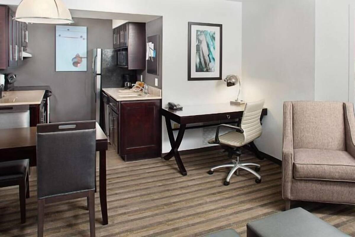 Habitación de hotel con cama, escritorio, silla, sofá, lámpara y un cuadro en la pared.