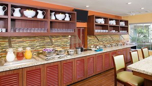 Ein Buffet mit verschiedenen Speisen, ein an der Wand befestigter Fernseher und eine Sitzecke mit Stühlen.