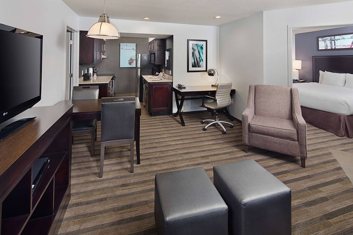 Una habitación de hotel con televisión, escritorio, silla, cama y kitchenette.