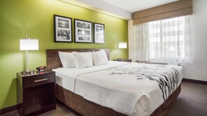 A hotel room with a large bed, a nightstand, a lamp, and a window with curtains.