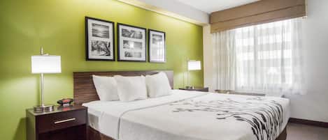 A hotel room with a large bed, a nightstand, a lamp, and a window with curtains.
