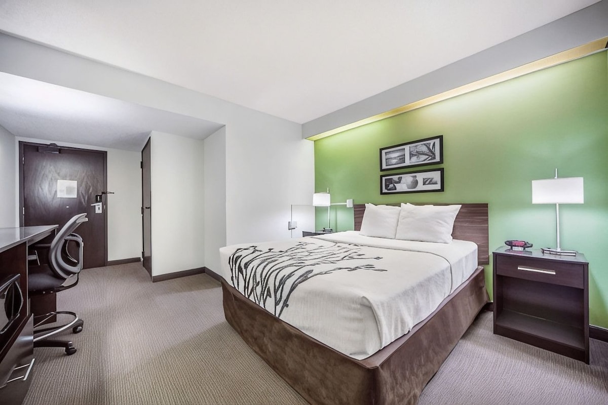 A hotel room with a bed, bedside tables, a desk, and chairs.