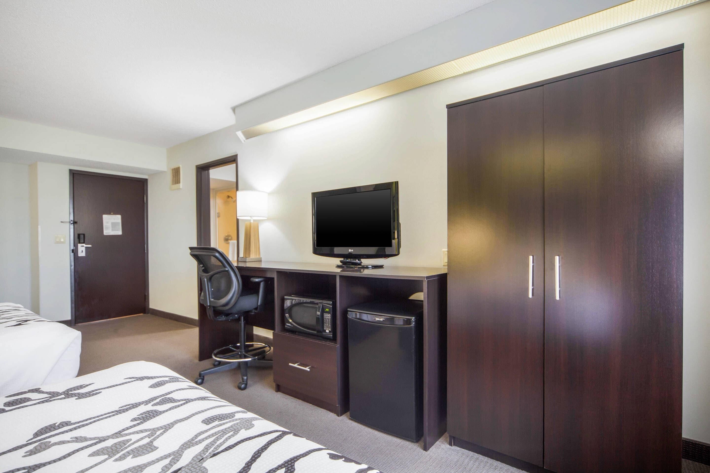 A hotel room with a bed, a desk with a television, a microwave, a refrigerator, and a wardrobe.