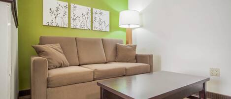 Una habitación con un sofá color beige, una mesa de centro de madera y una lámpara. Hay tres obras de arte colgadas en la pared sobre el sofá.