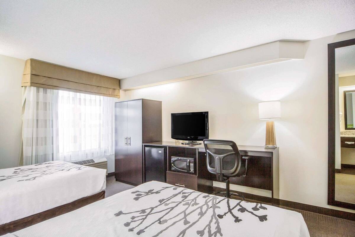 A hotel room with two beds, a desk with a TV, a refrigerator, and a mirror.