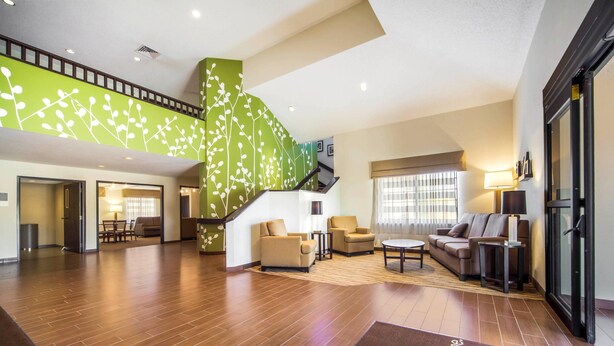 A spacious lobby with a wooden floor, a staircase with a green wall, and a reception desk.