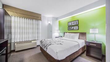 A hotel room with a large bed, a bedside table with a lamp, a heater, a window with curtains, and green walls.