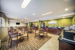 A hotel dining area with multiple tables and chairs, a kitchen counter, and a television mounted on the wall. - Sleep Inn & Suites Columbus, NE (Columbus)