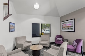 A modern lounge area with a round coffee table, grey upholstered chairs, a purple armchair, and a framed cityscape picture on the wall. - Sleep Inn Charleston North (Charleston)