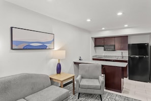 A compact hotel room with a sofa, a small table with a lamp, a kitchenette with a refrigerator, and a TV.