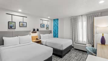 Habitación de hotel con dos camas, un escritorio, una silla, una mesita de noche, una lámpara, teléfono en la pared y una ventana con cortinas.