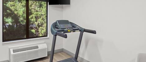 A treadmill in a room with a large window, a wall-mounted TV, and an air conditioning unit.