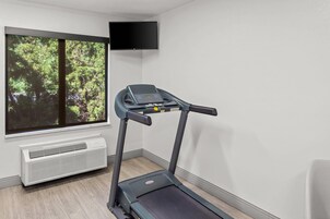 A treadmill in a room with a large window, a wall-mounted TV, and an air conditioning unit.