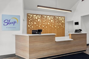 Un comptoir d’accueil d’hôtel avec un panneau décoratif en bois, un ordinateur Dell et un panneau indiquant « Sleep by Choice Hotels ».