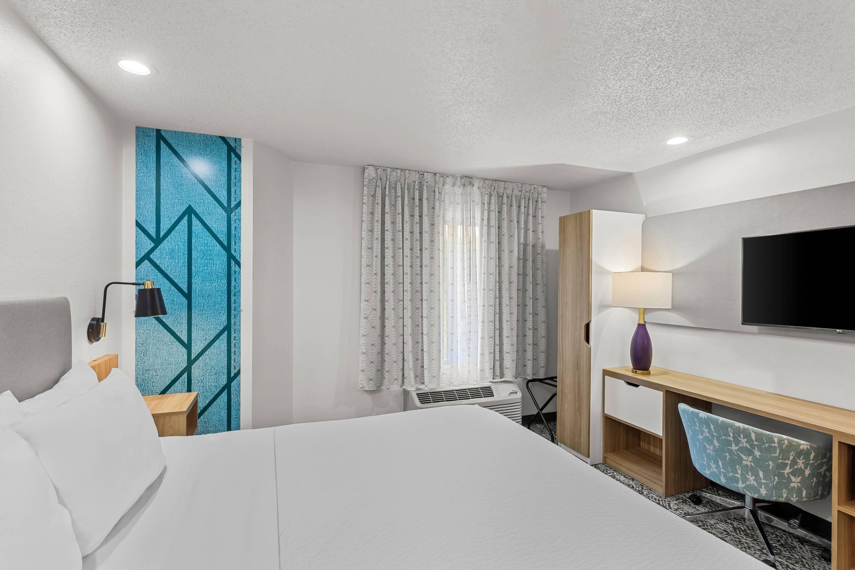 A hotel room with a bed, a desk, a chair, a TV, and a window with curtains.