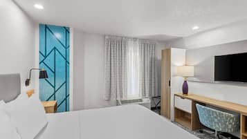 A hotel room with a bed, a desk, a chair, a TV, and a window with curtains.