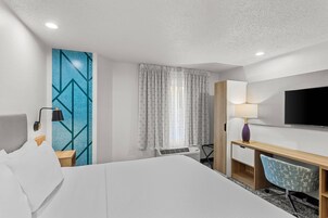 A hotel room with a bed, a desk, a chair, a TV, and a window with curtains.