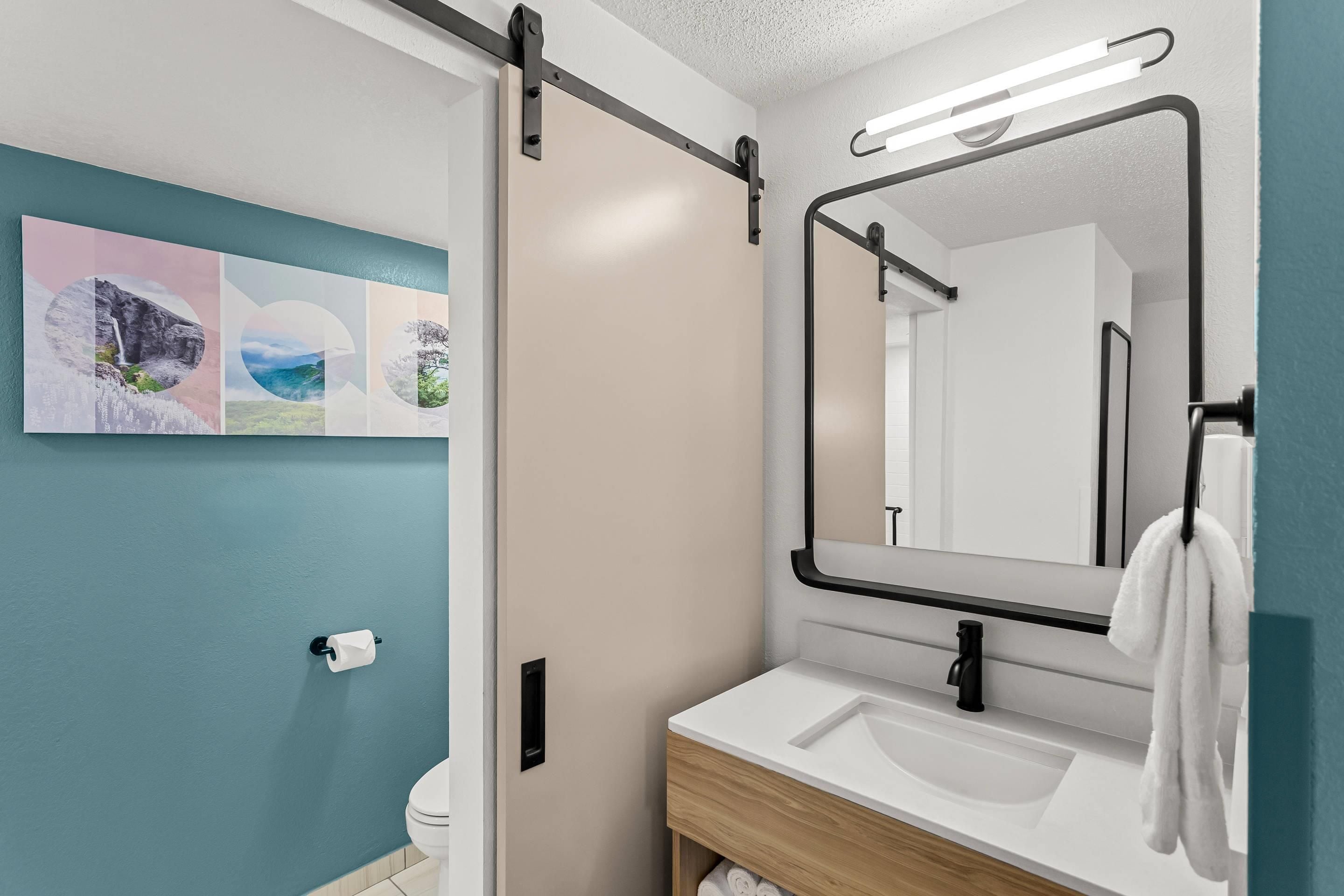 A bathroom with a toilet, sink, and mirror. There is a towel hanging on the wall.