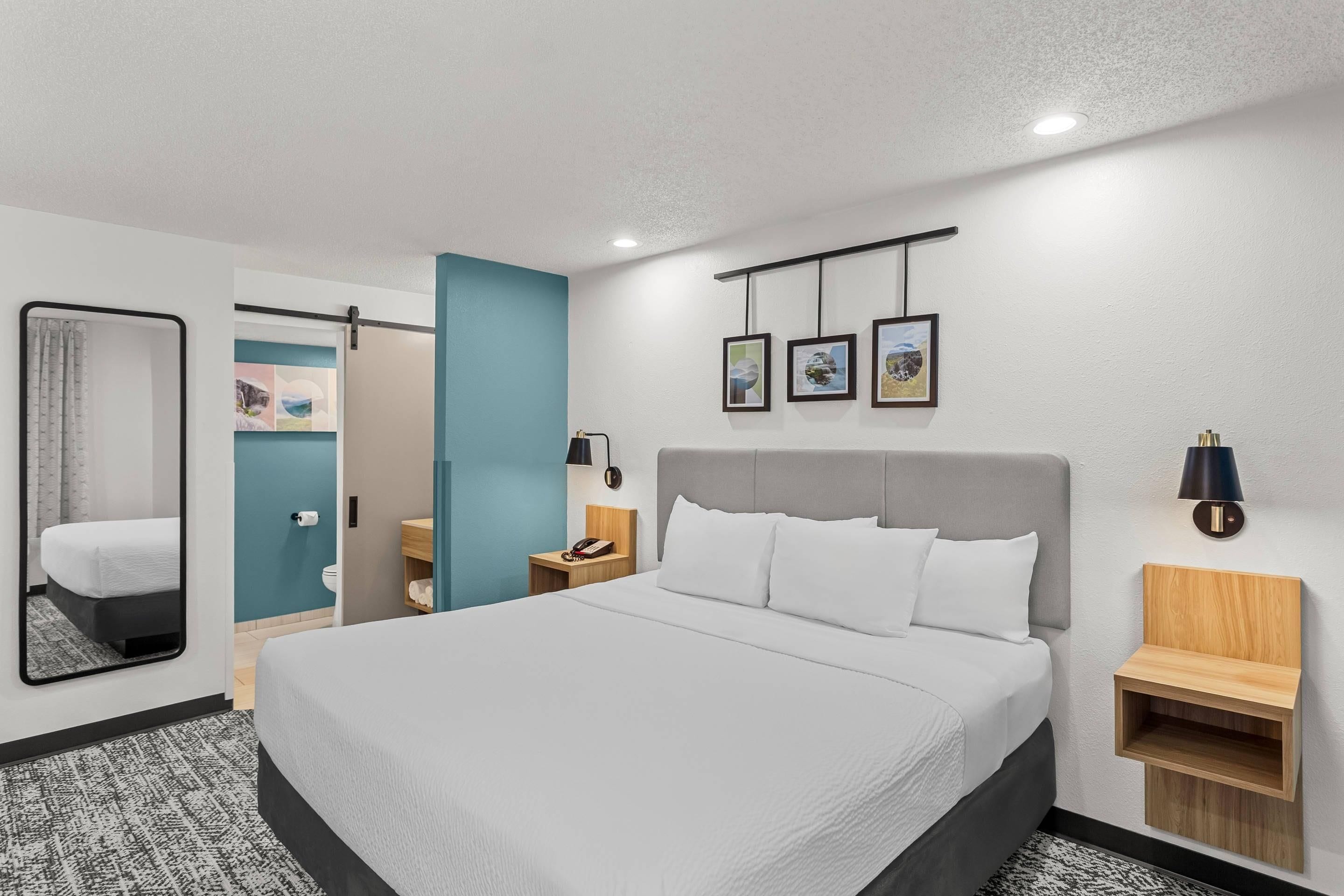 Una habitación de hotel con una cama grande, una mesita de noche, un espejo y una pared con tres cuadros enmarcados.