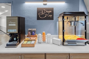 Estação de café com máquina de café, máquina de pipoca e uma placa que diz 'Dream Cup'.
