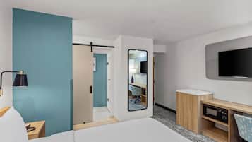 Una habitación de hotel con una cama, un escritorio, un televisor y un espejo.