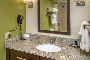 Casa de banho com bancada de granito, lavatório branco, secador de cabelo, porta-toalhas e espelho.