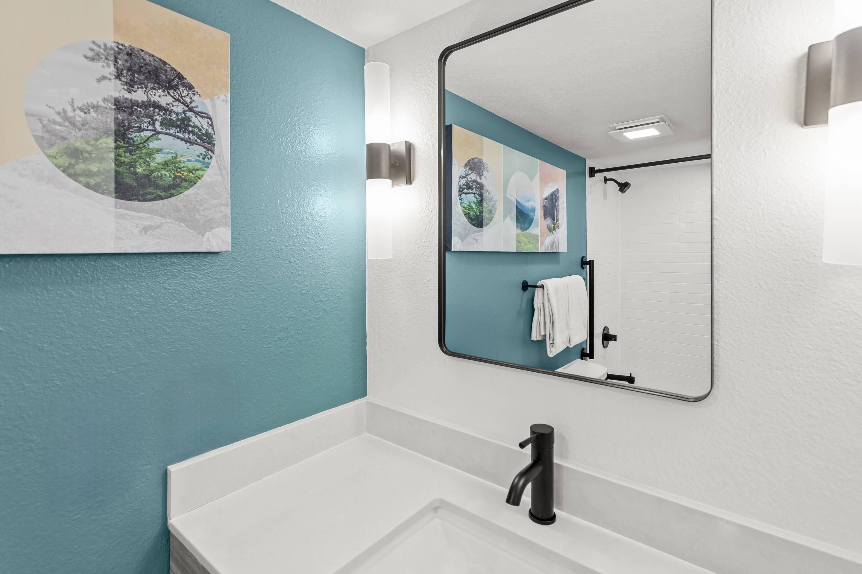 Un baño con un lavamanos blanco, un grifo negro y un espejo que refleja una zona de ducha.