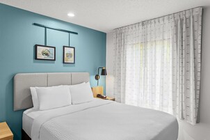 Habitación de hotel con cama, mesita de noche, lámpara y dos cuadros en la pared.