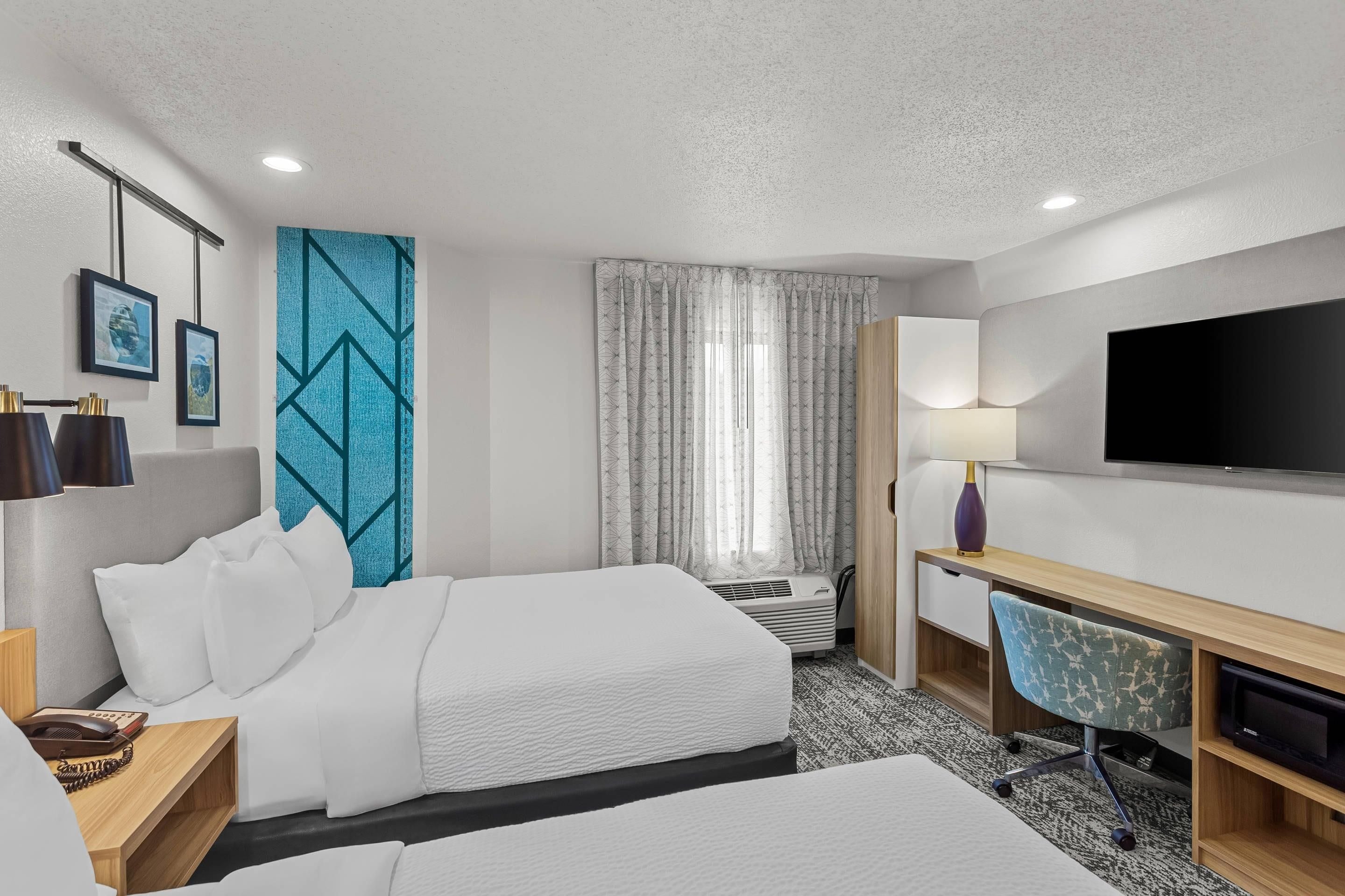 A hotel room with two beds, a desk, a television, and a window with curtains.