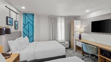 A hotel room with two beds, a desk, a television, and a window with curtains.