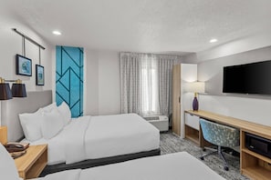 A hotel room with two beds, a desk, a television, and a window with curtains.