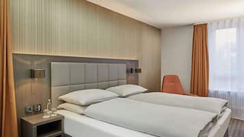 Habitación de hotel con una cama grande, una mesita de noche con lámpara, una silla y vistas al exterior a través de la ventana.
