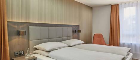 A hotel room with a large bed, a bedside table with a lamp, a chair, and a view of the outdoors through the window.