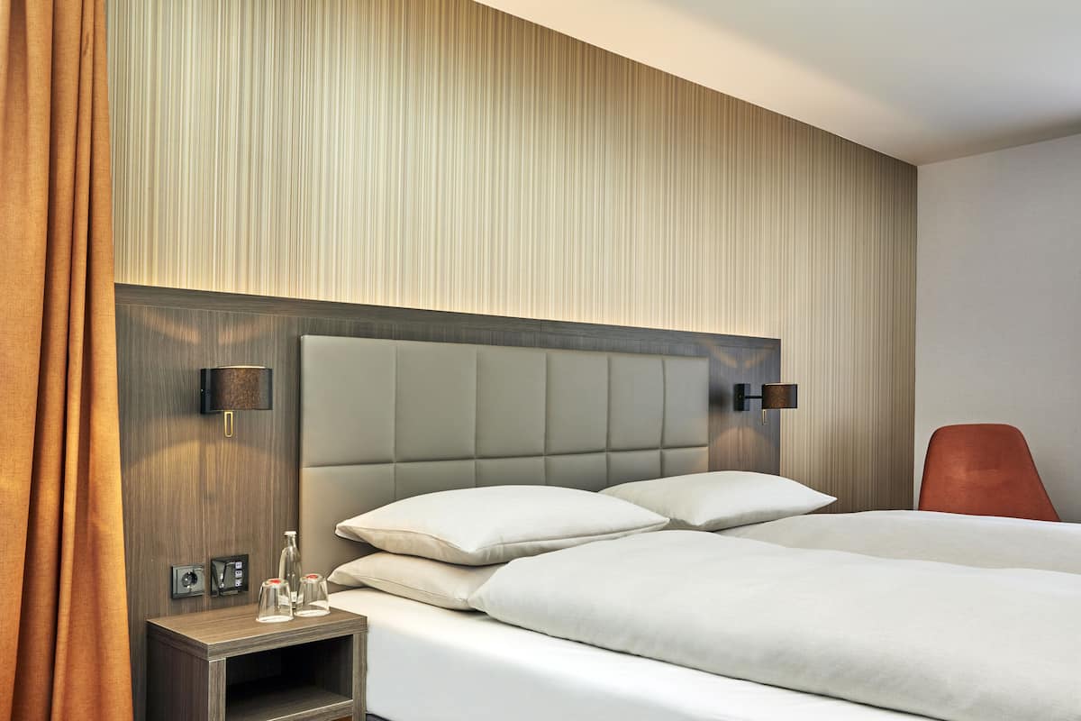 Une chambre d’hôtel avec un grand lit, une table de chevet, une lampe et un fauteuil rouge.