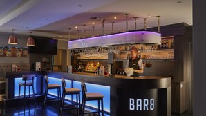 A modern bar area with a bar counter, stools, and a bartender.