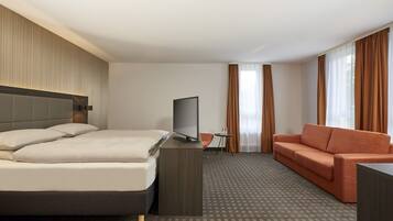 Ein Hotelzimmer mit Bett, Fernseher, Sofa und Schreibtisch.