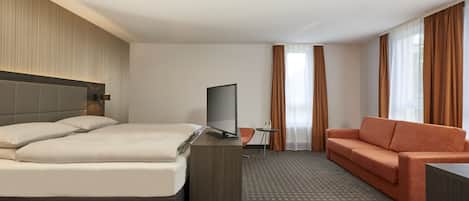 Una habitación de hotel con cama, televisión, sofá y escritorio.