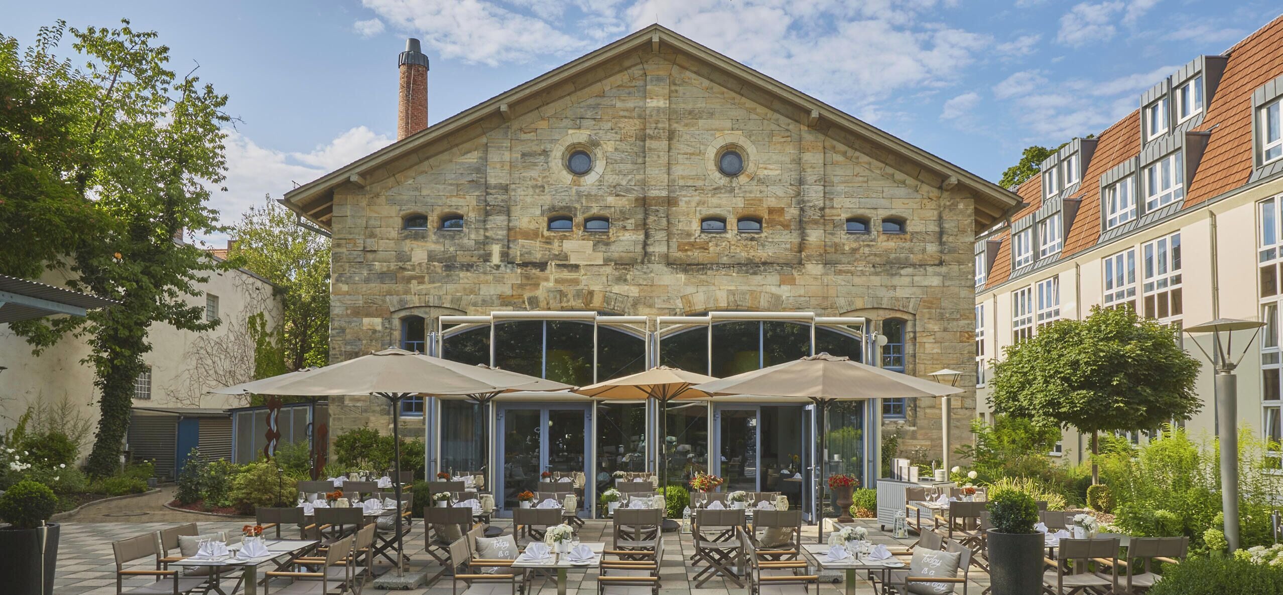 A stone building with a large patio area featuring outdoor seating and umbrellas.